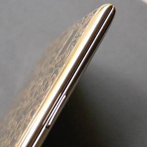 May include: A silver and gold smartphone with a decorative pattern on the back. The phone is closed and the screen is not visible.