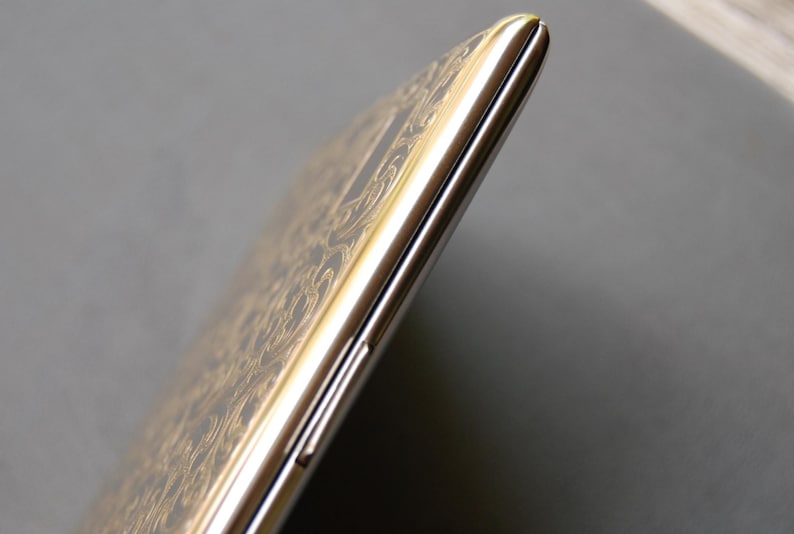 May include: A silver and gold smartphone with a decorative pattern on the back. The phone is closed and the screen is not visible.