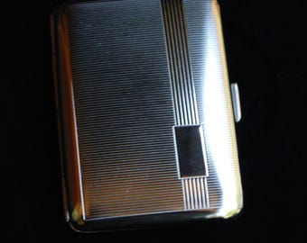 May include: A silver cigarette case with a textured surface and a decorative design. The case has a hinged lid and a small latch.