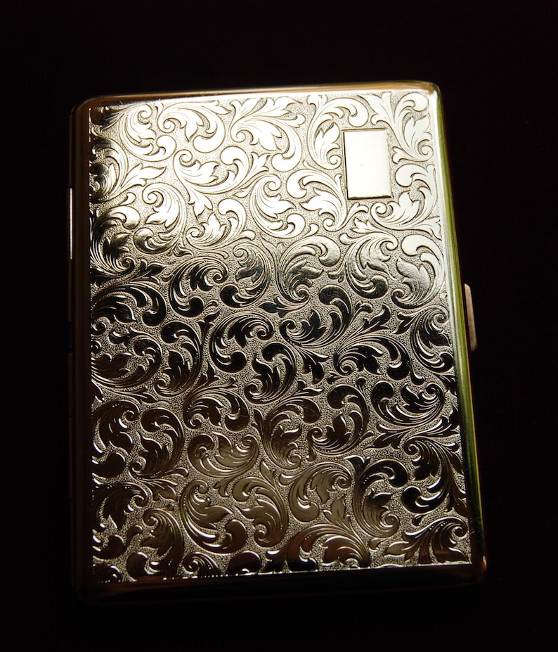 May include: A silver cigarette case with an ornate floral design.
