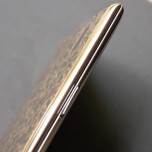 May include: A gold smartphone with a patterned design on the back. The phone is shown from the side, with the volume buttons and power button visible.