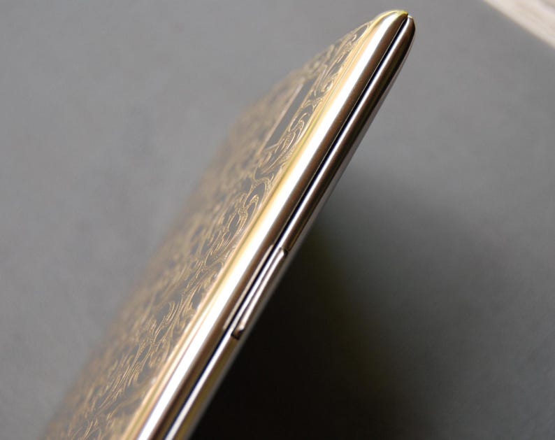 May include: A gold smartphone with a patterned design on the back. The phone is shown from the side, with the volume buttons and power button visible.