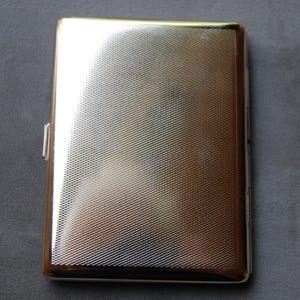 May include: A silver cigarette case with a textured surface.