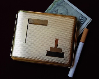 Peut inclure: Un étui à cigarettes en métal doré avec une surface texturée et un motif géométrique. L'étui est fermé et possède une charnière sur le côté.