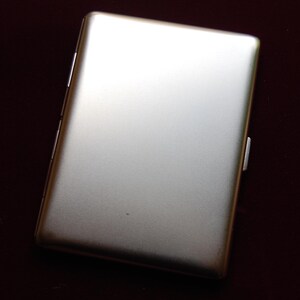 May include: A silver metal cigarette case with a smooth, brushed finish.