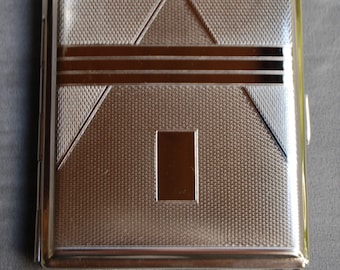 May include: A silver cigarette case with a geometric design and a textured surface.