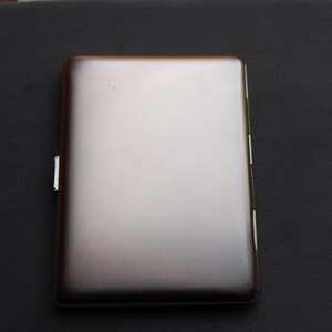 May include: A silver cigarette case with a smooth, metallic finish.