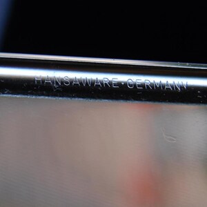 May include: Close-up of a silver metal container with the inscription "Hansaware Germany" on the edge.
