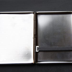 May include: A silver metal cigarette case with a black elastic band.