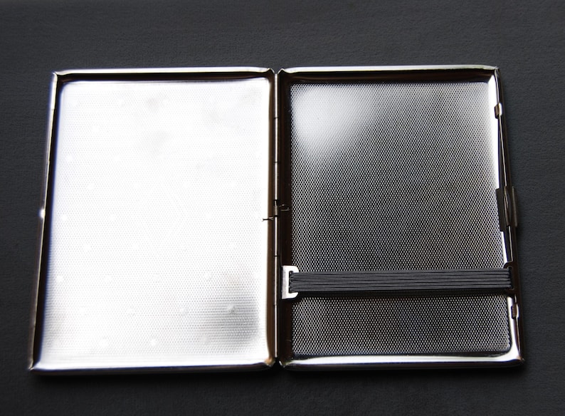 May include: A silver metal cigarette case with a black elastic band.