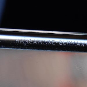 Peut inclure: Gros plan d'un objet en m&eacute;tal argent&eacute; avec l'inscription "HANSWARE - GERMANY" sur le c&ocirc;t&eacute;.