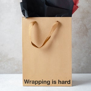 A funny gift bag made from eco-friendly brown kraft paper with "wrapping is hard" written on the front