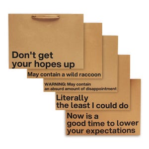 Op de afbeelding: Een stapel bruine papieren cadeauzakjes met humoristische zwarte tekst. De bovenste zak leest "Don't get your hopes up". Andere zinnen zijn "May contain a wild raccoon" en "Now is a good time to lower your expectations."