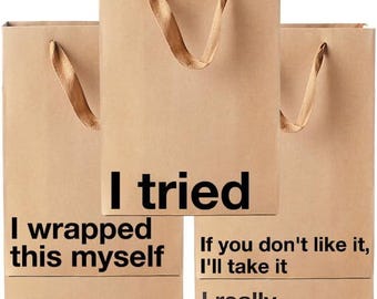 Könnte beinhalten: Drei hellbraune Geschenktüten aus Papier mit braunen Bandgriffen. Die Tüten sind mit schwarzem Text bedruckt: I tried, I wrapped this myself, It was on sale, If you don't like it, I'll take it und I really shouldn't have. Die Tüten sind rechteckig.
