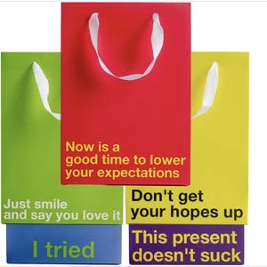 May include: Four colorful gift bags stacked on top of each other. The top bag is red with white handles and the text "Now is a good time to lower your expectations". The second bag is green with white handles and the text "Just smile and say you love it". The third bag is yellow with white handles and the text "Don't get your hopes up". The bottom bag is purple with the text "This present doesn't suck".