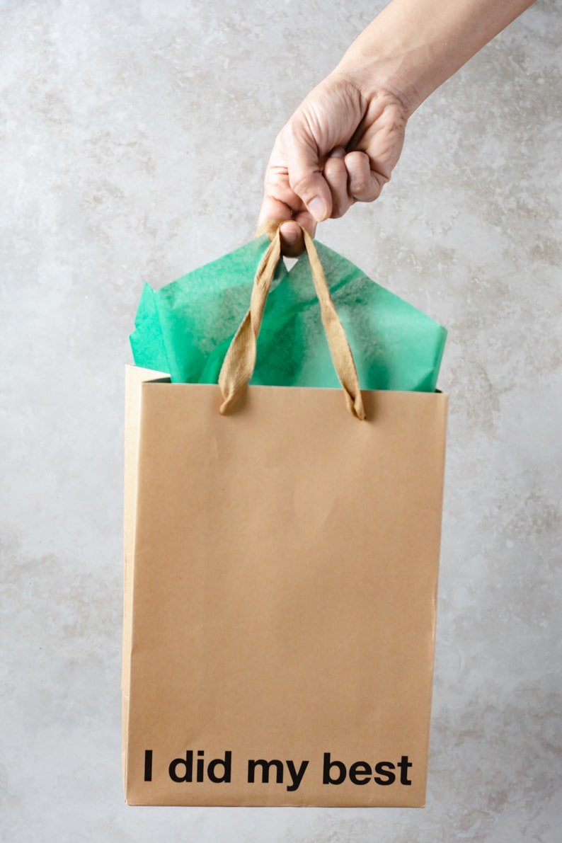 May include: A brown paper shopping bag with a green tissue paper peeking out of the top. The bag has a brown handle and the text "I did my best" printed on the bottom.
