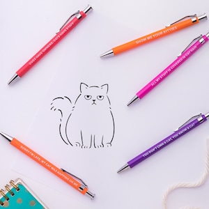 May include: Six colourful pens with humorous cat-themed sayings. The pens are on a white background with a simple line drawing of a cat.