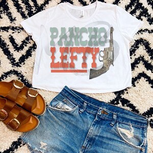 May include: White cropped t-shirt with the text "Pancho Lefty" in red and green lettering. A stylised image of a revolver is behind the text.