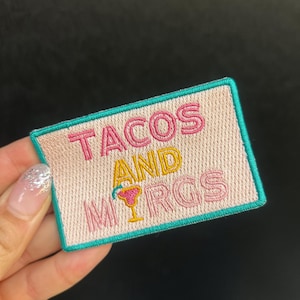 Peut inclure: Écusson brodé avec les mots "TACOS AND MRGS" en lettres roses et jaunes. L'écusson a un fond rose clair avec une bordure turquoise et un graphique de cocktail. L'écusson est rectangulaire.