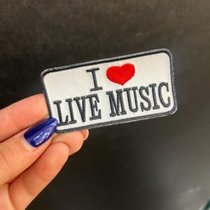 May include: A rectangular patch with the words "I LOVE LIVE MUSIC" in black letters. A red heart replaces the word "love". The patch has a white background and a black border.