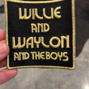 Puede incluir: Parche de tela negro con texto bordado en dorado que dice "Willie and Waylon and the Boys".