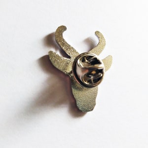 May include: Silver metal pin with a deer head design. The pin has a safety clasp on the back.