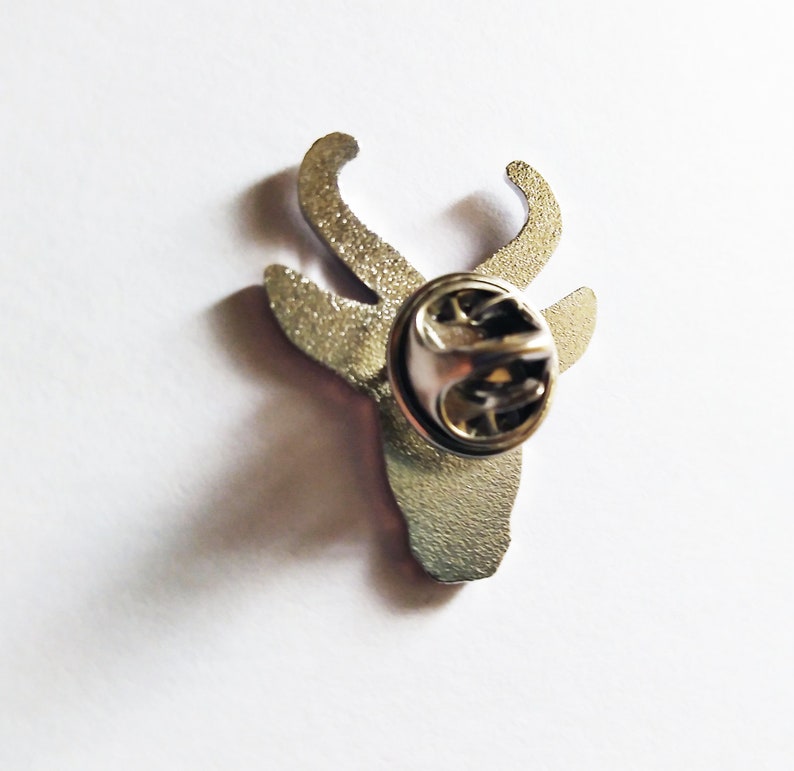 May include: Silver metal pin with a deer head design. The pin has a safety clasp on the back.