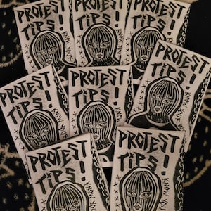 Könnte beinhalten: Eine Sammlung von Zines mit dem Titel "PROTEST TIPS!" mit einer Schwarz-Weiß-Illustration einer Person mit Sturmhaube. Der Text "KNOW YOUR RIGHTS" ist ebenfalls sichtbar. Die Zines sind fächerförmig angeordnet.