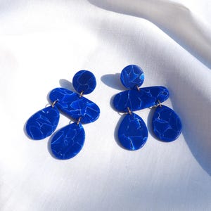 May include: A pair of blue statement earrings with a marbled effect. The earrings are made of multiple geometric shapes, including circles, ovals, and teardrops.