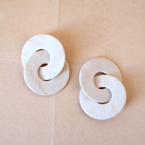 Puede incluir: Un par de pendientes de mármol blanco con un diseño de círculo enlazado.