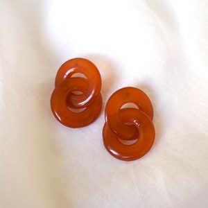 May include: A pair of amber-colored resin earrings with a linked circle design.