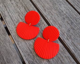 Peut inclure: Une paire de boucles d'oreilles semi-circulaires rouges avec une texture en éventail. Les boucles d'oreilles sont en argile polymère et ont un crochet en métal doré.