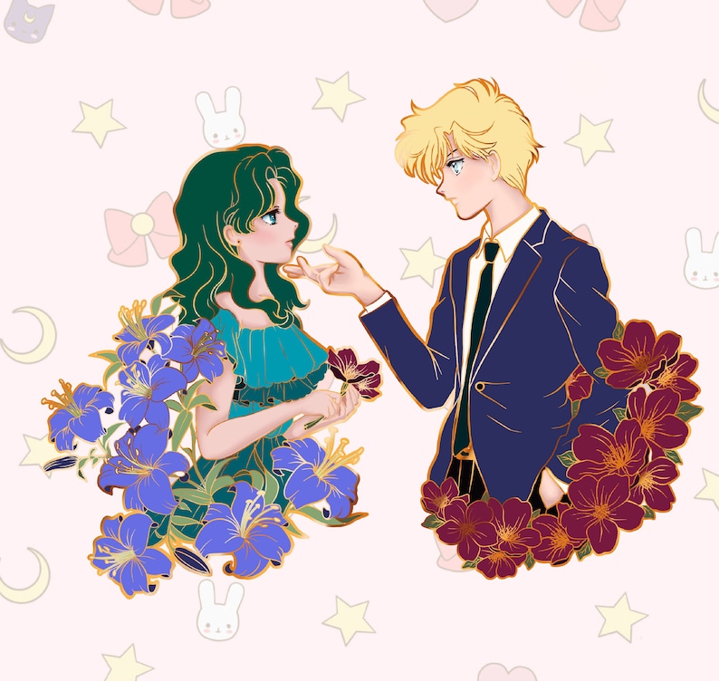 Op de afbeelding: Een gouden emaille pin met een stel in een romantische pose. De vrouw heeft groen haar en draagt een blauwe jurk. De man heeft blond haar en draagt een blauw pak. Beide zijn omringd door paarse en rode bloemen.