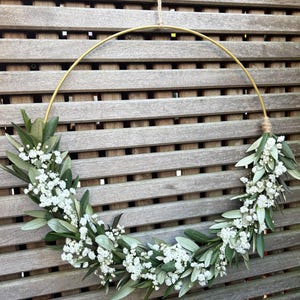 May include: A gold metal hoop wreath decorated with white baby's breath flowers and green foliage.