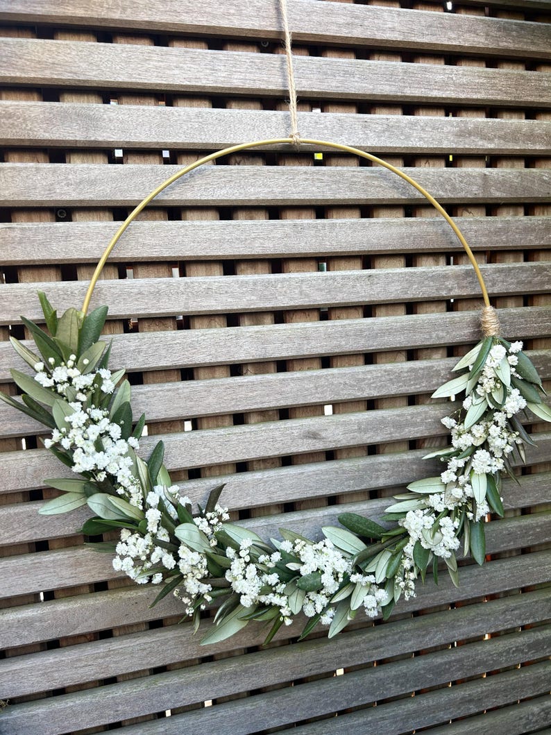 May include: A gold metal hoop wreath decorated with white baby's breath flowers and green foliage.