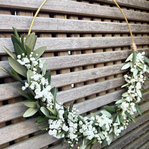 May include: A gold metal hoop wreath decorated with white baby's breath flowers and green foliage.