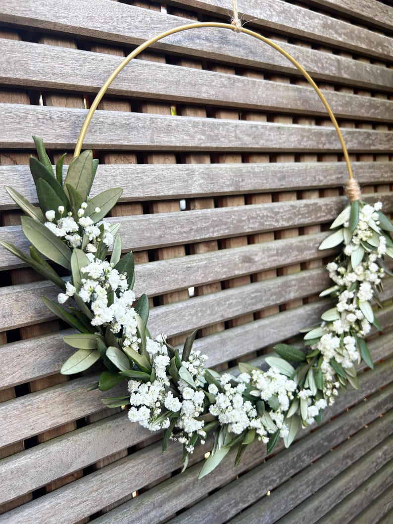 May include: A gold metal hoop wreath decorated with white baby's breath flowers and green foliage.