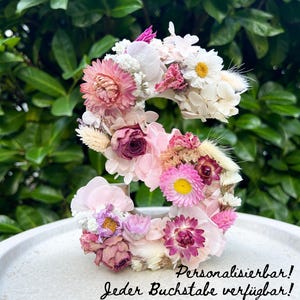 Könnte beinhalten: Ein floraler Buchstabe "S" aus getrockneten Blumen in Rosa-, Weiß- und Gelbtönen. Der Buchstabe steht auf einer weißen Oberfläche, mit grünem Laub im Hintergrund. Der Text im Bild lautet "Personalisierbar! Jeder Buchstabe verfügbar!"