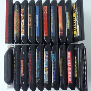 May include: A selection of black video game cartridges, including titles such as "Sonic the Hedgehog 2", "Batman Forever", and "The Lost World: Jurassic Park". The cartridges are displayed in two rows, with vibrant labels.