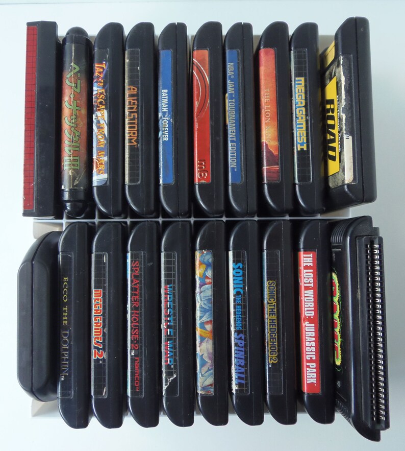 May include: A selection of black video game cartridges, including titles such as "Sonic the Hedgehog 2", "Batman Forever", and "The Lost World: Jurassic Park". The cartridges are displayed in two rows, with vibrant labels.