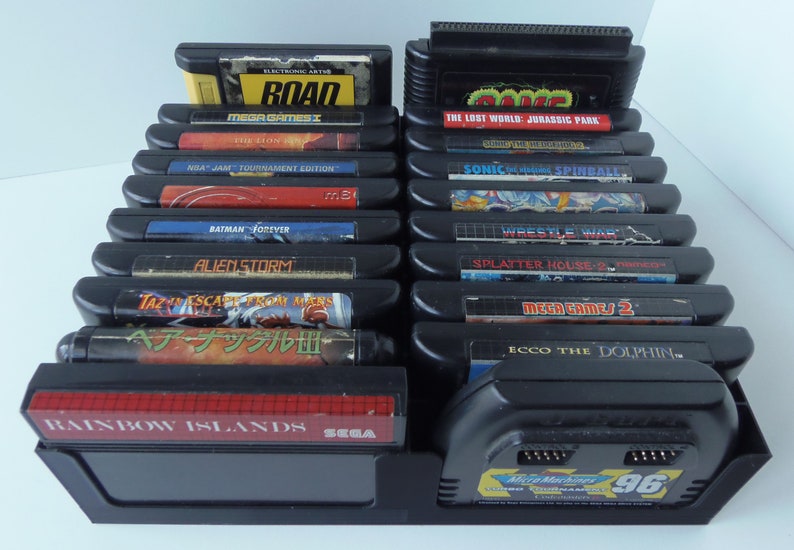 May include: A selection of black Sega Genesis video game cartridges, featuring titles such as "Road," "Sonic Spinball," and "Batman Forever." The cartridges are displayed in a black stand, with various game labels visible.