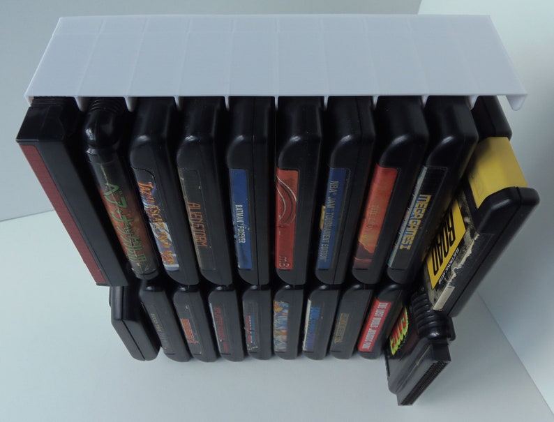 May include: A white plastic video game cartridge holder filled with black game cartridges. The cartridges have colourful labels with game titles. The holder is designed to keep the cartridges organised and accessible.