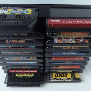 May include: A collection of black Sega Genesis game cartridges, featuring titles such as "Micro Machines 96", "Rainbow Islands", and "The Lost World: Jurassic Park". The cartridges are stored in a black plastic holder.