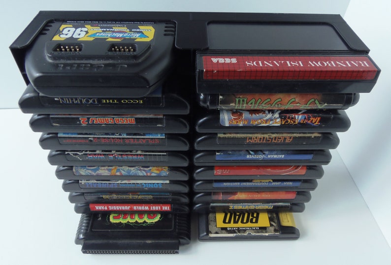 May include: A collection of black Sega Genesis game cartridges, featuring titles such as "Micro Machines 96", "Rainbow Islands", and "The Lost World: Jurassic Park". The cartridges are stored in a black plastic holder.