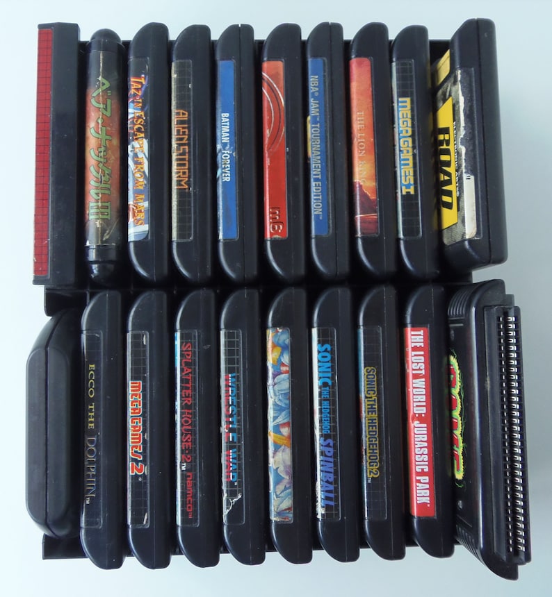 May include: A selection of black Sega Genesis video game cartridges in a black rack. Titles include "Alien Storm", "Batman Forever", "Sonic the Hedgehog 2", and "The Lost World: Jurassic Park".