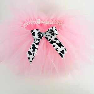 May include: A pink tulle tutu with a black and white cow print bow.