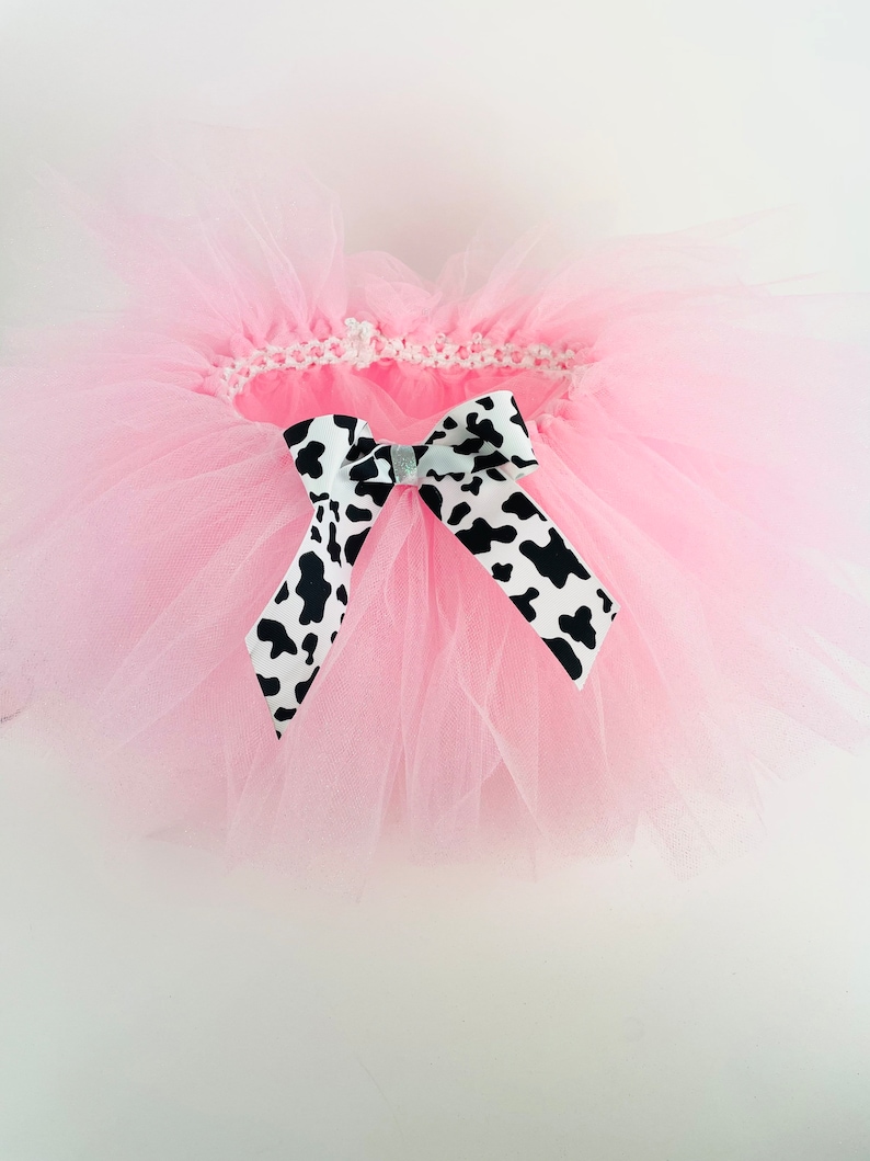 May include: A pink tulle tutu with a black and white cow print bow.