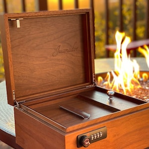 May include: A wooden box with a combination lock and a leather-lined interior. The box is labelled "Juanador" and is open, revealing a compartment with a metal slide.