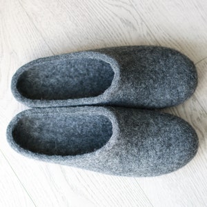 Könnte beinhalten: Ein Paar graue Filzpantoffeln. Die Pantoffeln sind weich und gemütlich, perfekt um die Füße im Winter warm zu halten.