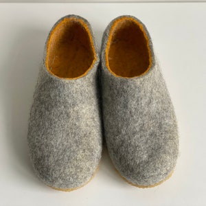 May include: A pair of grey felt slippers with a yellow lining. The slippers are soft and cosy, perfect for keeping your feet warm in the winter.